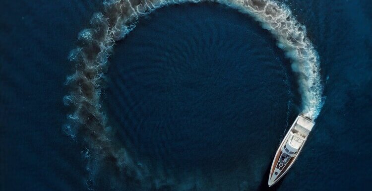 una nave naviga tra le onde del mare blu formando, con la sua scia, un cerchio sull'acqua