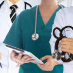 immagine con primo piano sul busto e sulle mani di tre medici con strumenti e cartelle cliniche in mano
